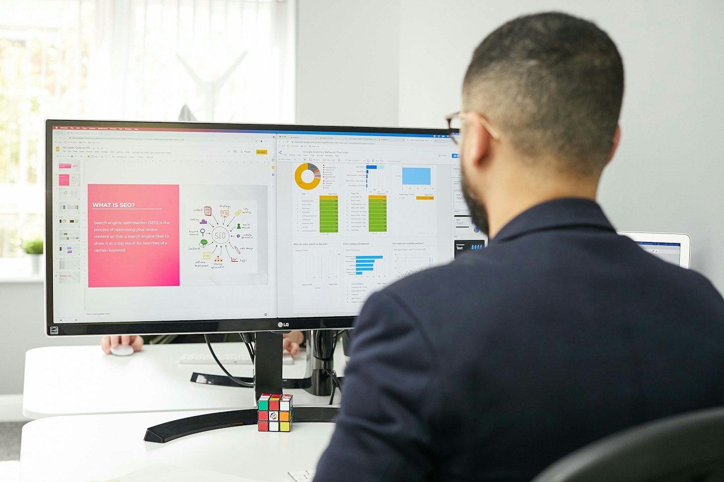Man works on dual computer monitors displaying SEO and analytics.